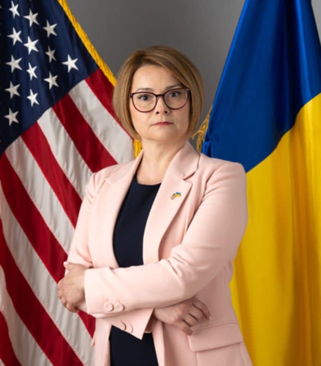 Maryna Baydyuk, President of United Help Ukraine, with Ukrainian and American flags behind.